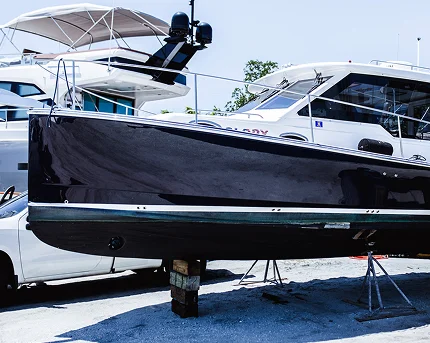 Black boat hull elevated on supports in a marina boatyard, positioned beside white yachts.