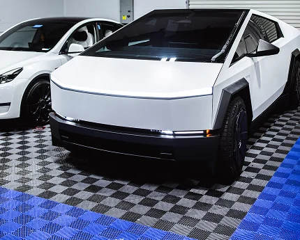White Tesla Cybertruck parked indoors beside a white Tesla Model X on a checkered garage floor.