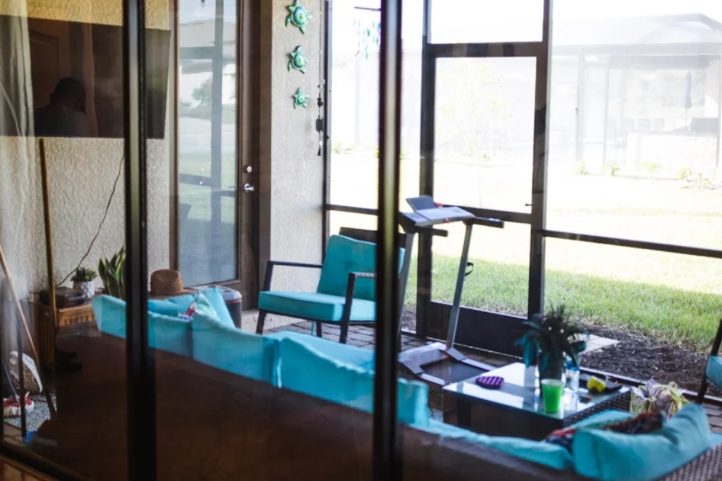 View of a sunroom with tinted windows and teal furniture, showcasing a stylish application of residential window tinting while hinting at potential drawbacks like reduced night visibility and the importance of professional installation.