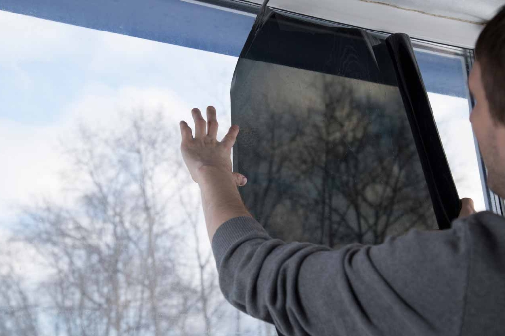A person carefully applies dark window film to a large residential window, demonstrating how to choose the right window film for privacy, UV protection, and impact resistance in Fort Myers homes.