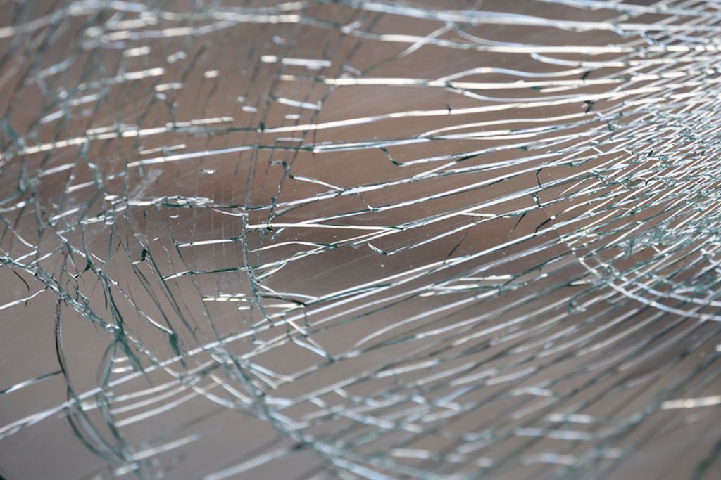 Close-up of shattered safety glass held together by protective window film, demonstrating how hurricane protection film helps prevent dangerous shards from scattering during storms.
