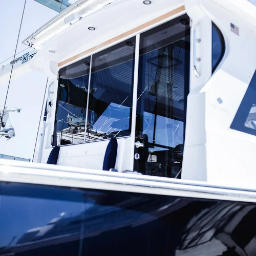 Close-up of a luxury yacht’s cabin with large tinted glass windows reflecting the marina surroundings. The boat’s sleek white and navy design highlights its modern styling.